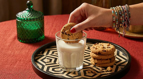 Indulgent Moment: Dipping a Chocolate Chip Cookie in Milk with Stylish Red Nail Art